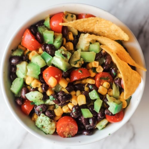 black bean corn salad win a white bowl garnished with tortilla chips