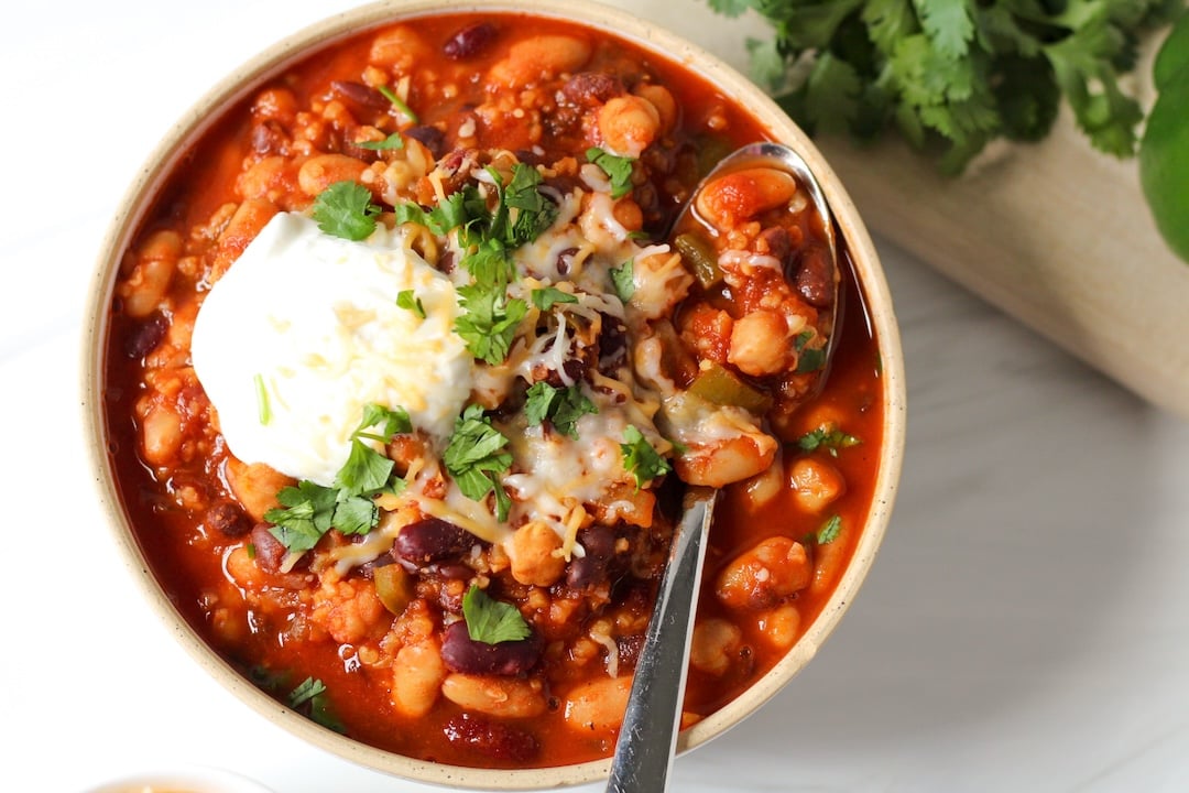 4 bean chili in a white bowl topped with Greek yogurt, cilantro, and cheese