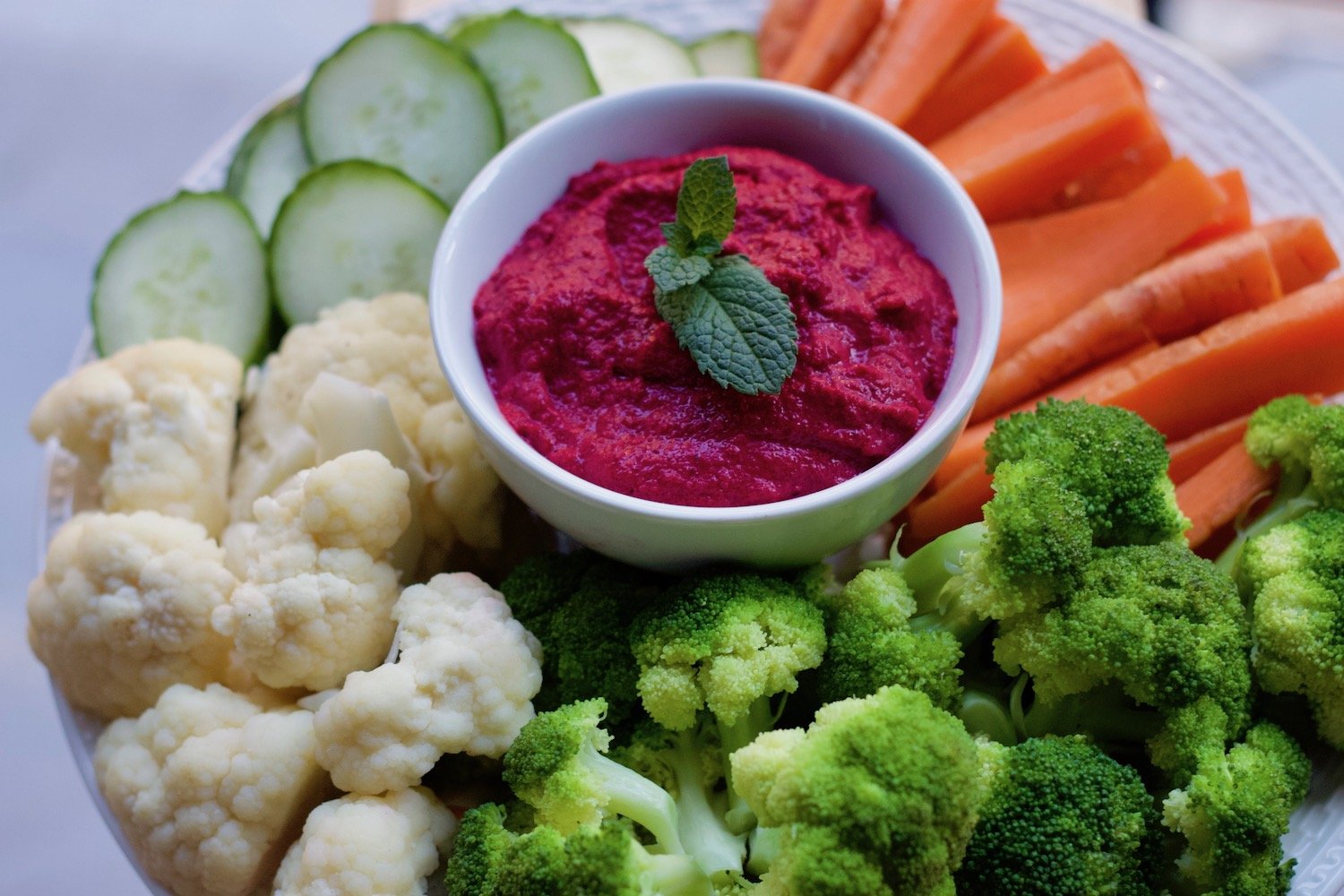 Organic food facts picture of cauliflower, broccoli, carrots, cucumber, beet hummus on a plate