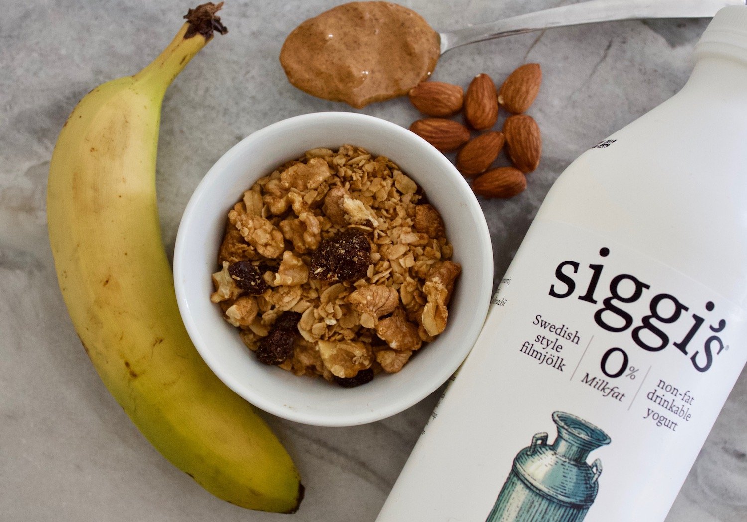 healthy breakfast - a bowl of homemade granola, banana, almonds, kefir, and a spoonful of almond butter