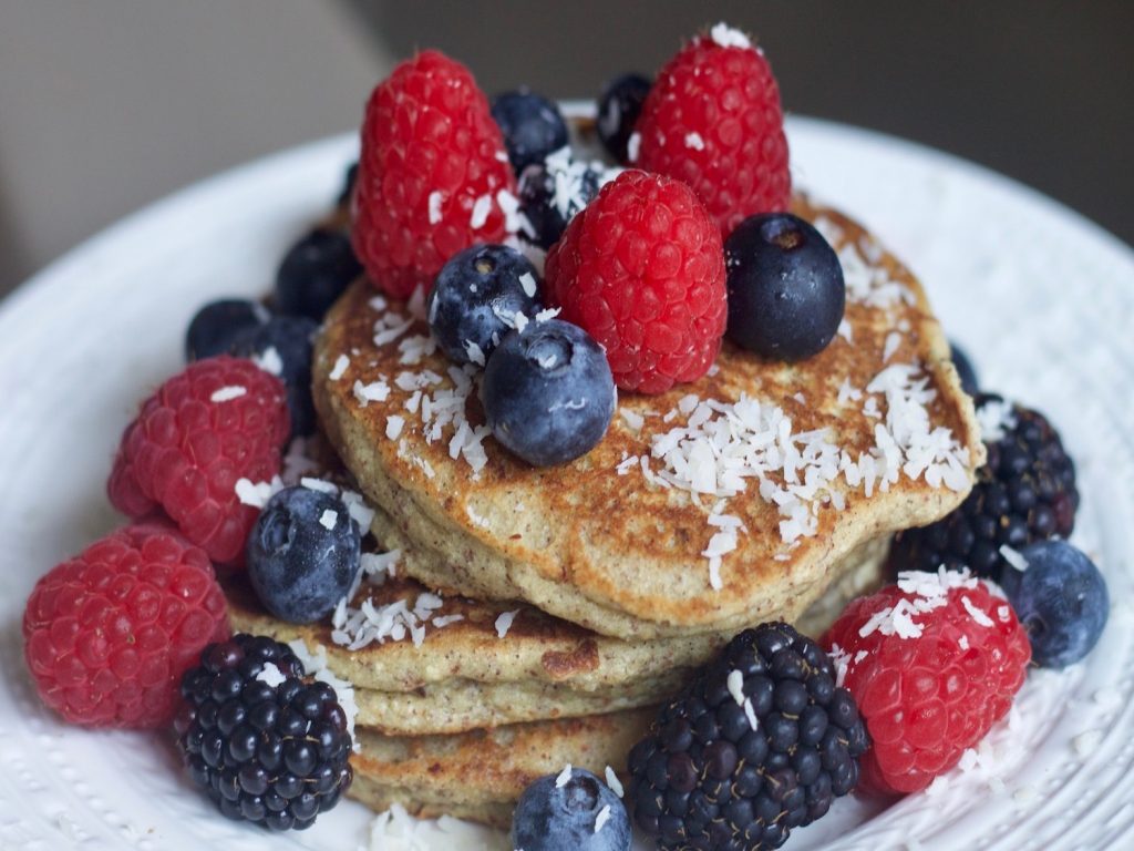 three whole wheat pancakes topped with fresh coconut and fresh berries