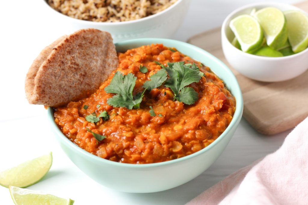 Creamy lentil curry in a bowl with a whole wheat pita triangle and sprinkle of cilantro