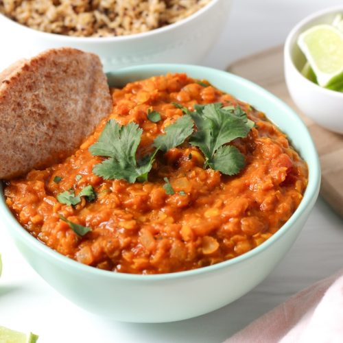 Creamy lentil curry in a bowl with a whole wheat pita triangle and sprinkle of cilantro