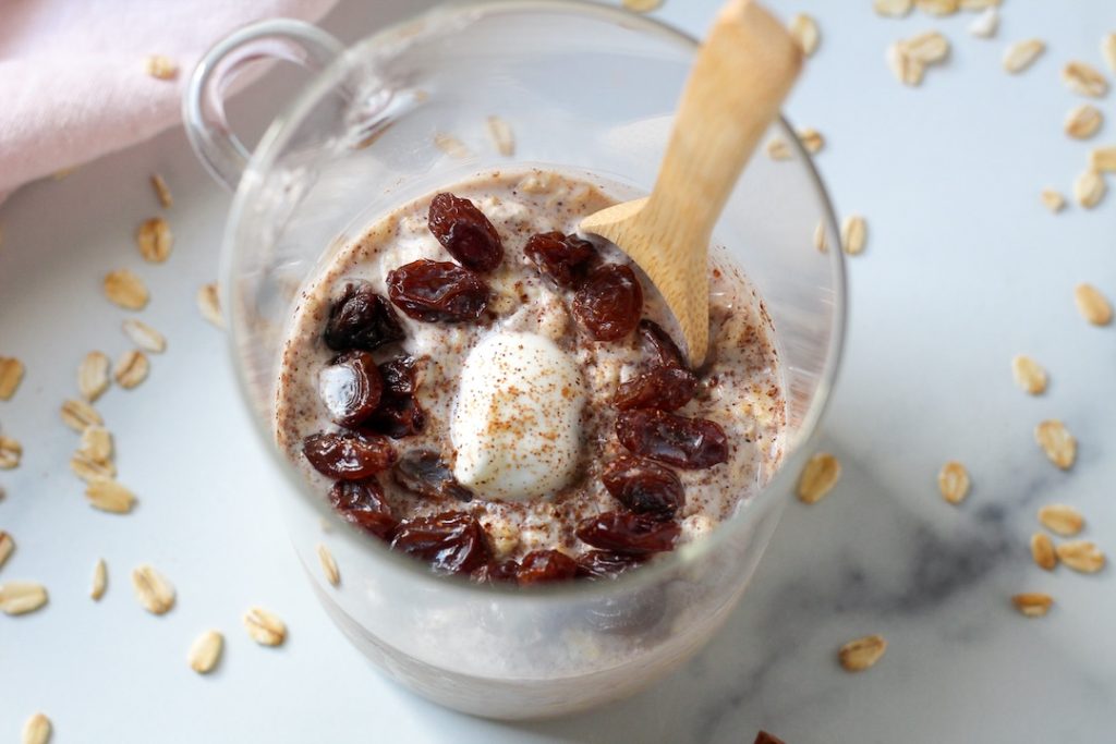Cinnamon overnight oats topped with raisins and yogurt in a clear mug