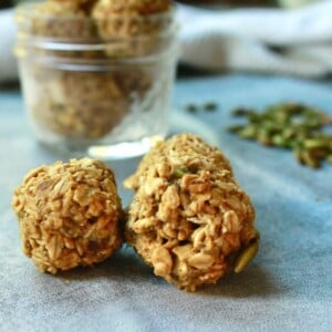 three pumpkin energy bites on a counter top with toasted pumpkin seeds in the background