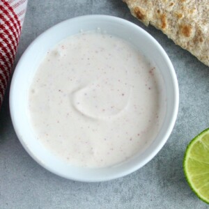 lime crema with greek yogurt in a small bowl with a lime wedge and a whole wheat tortilla