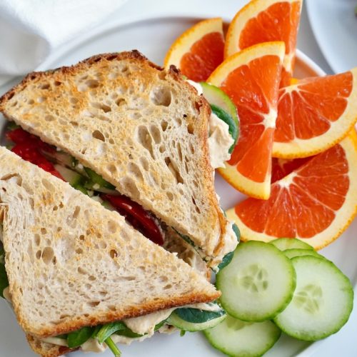 hummus sandwich on a plate with orange slices and cucumber slices