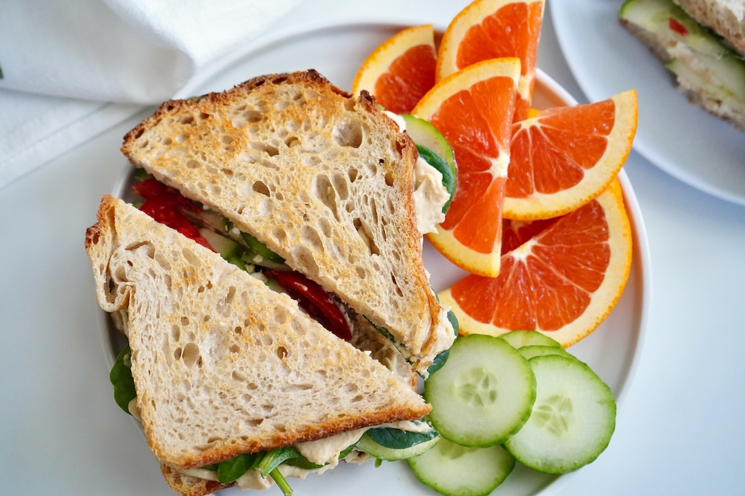hummus sandwich on a plate with orange slices and cucumber slices
