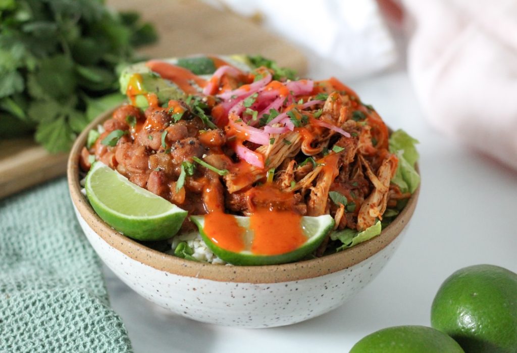 chicken burrito bowl with rice and beans in a bowl with lime and hot sauce