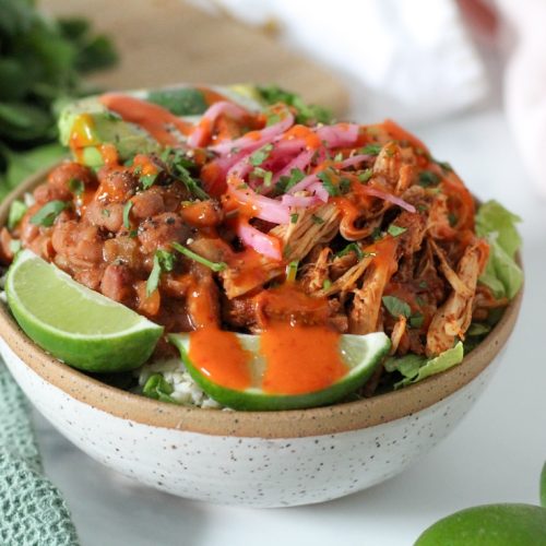 chicken burrito bowl with rice and beans in a bowl with lime and hot sauce