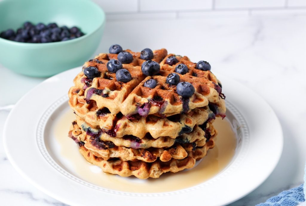 Stack of blueberry waffles on a white plate with maple syrup