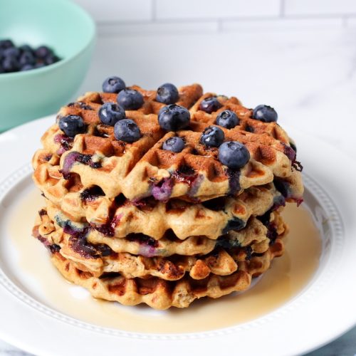 Stack of blueberry waffles on a white plate with maple syrup