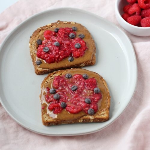 Whole wheat toast spread with peanut butter, topped with mashed raspberries, and sprinkled with chocolate chips