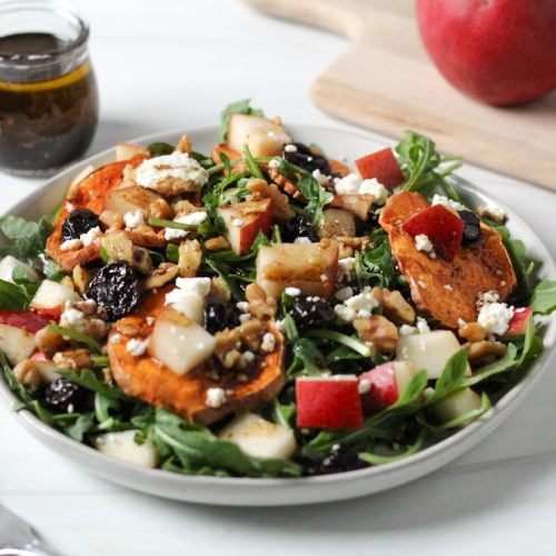 Goat cheese pear salad with sweet potato crisps, dried cherries, and arugula in a white bowl