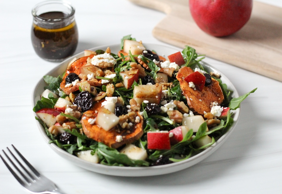 Goat cheese pear salad with sweet potato crisps, dried cherries, and arugula in a white bowl