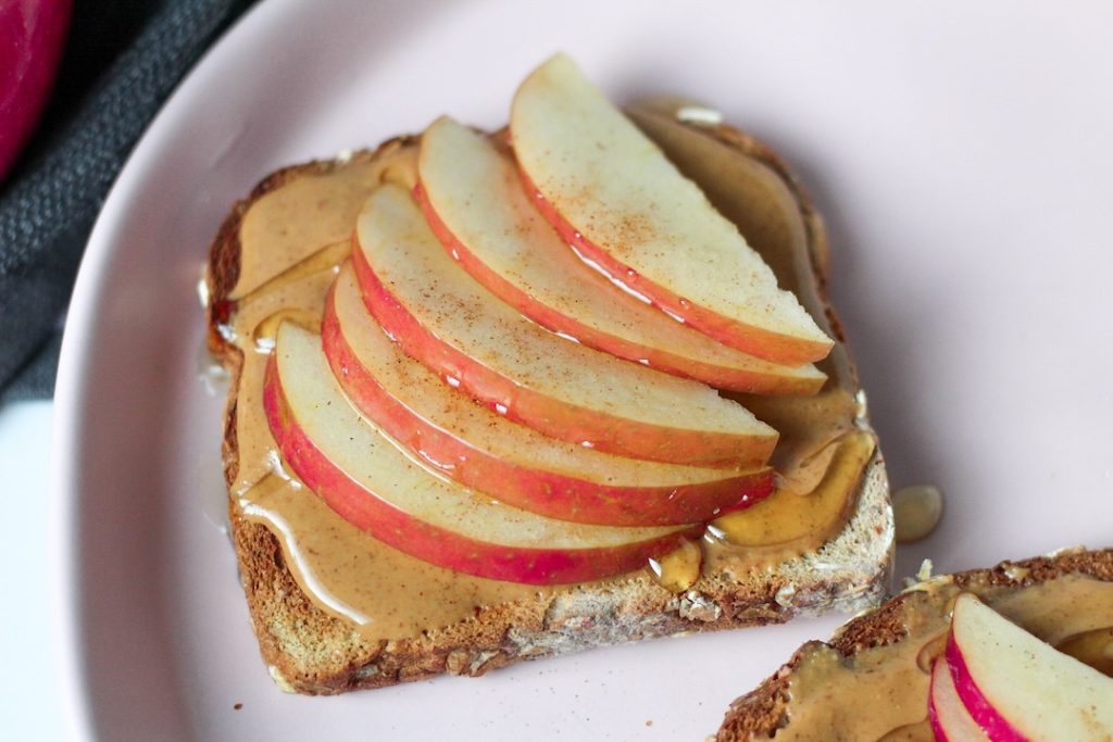 Peanut butter spread on whole grain toast, topped with sliced apples and honey