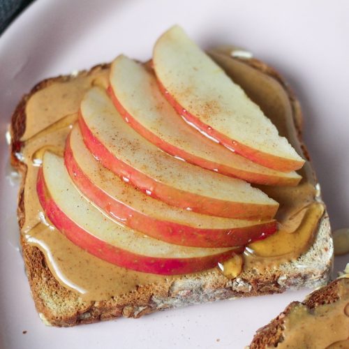 Peanut butter spread on whole grain toast, topped with sliced apples and honey