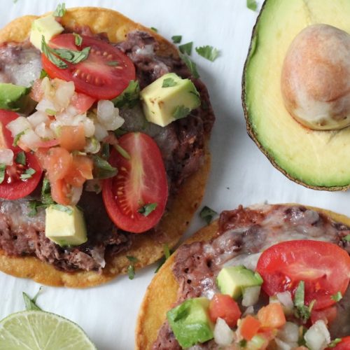 2 black bean and tomato tostadas with an avocado half nearby