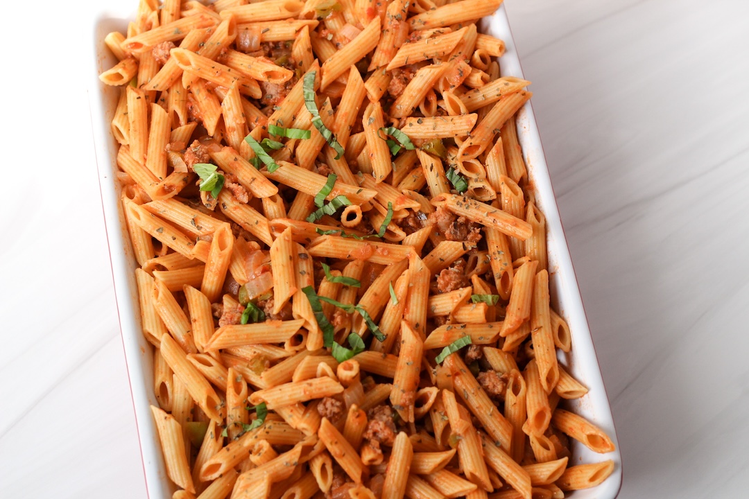 Penne pasta with sausage, peppers, and onions in a white rectangular serving dish