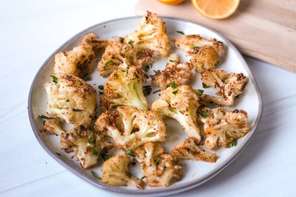 Parmesan roasted cauliflower on a plate with a cut lemon nearby