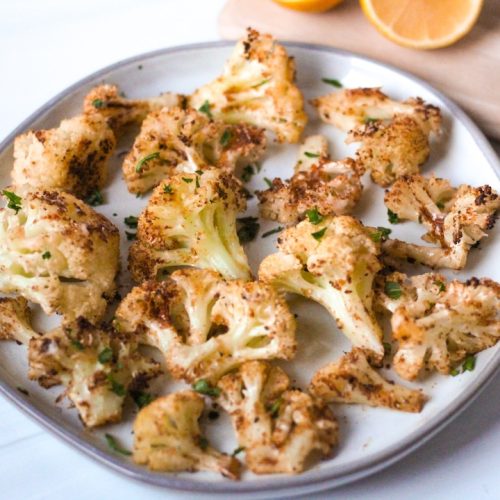 Parmesan roasted cauliflower on a plate with a cut lemon nearby
