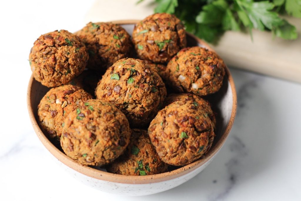 9 lentil meatballs in a white bowl with a sprig of parlsey in the top right corner on the counter.