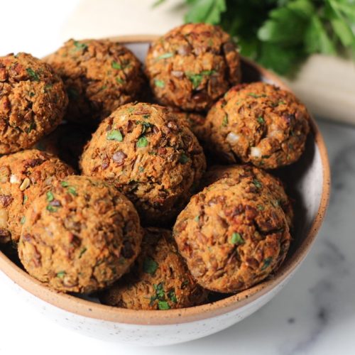 9 lentil meatballs in a white bowl with a sprig of parlsey in the top right corner on the counter.